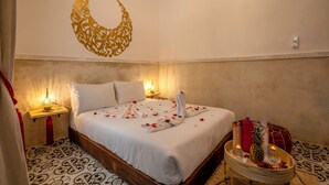 Ein Hotelzimmer mit Bett, Wanddekoration, Nachttisch mit Lampe und Tablett mit Kerzen und Ananas.