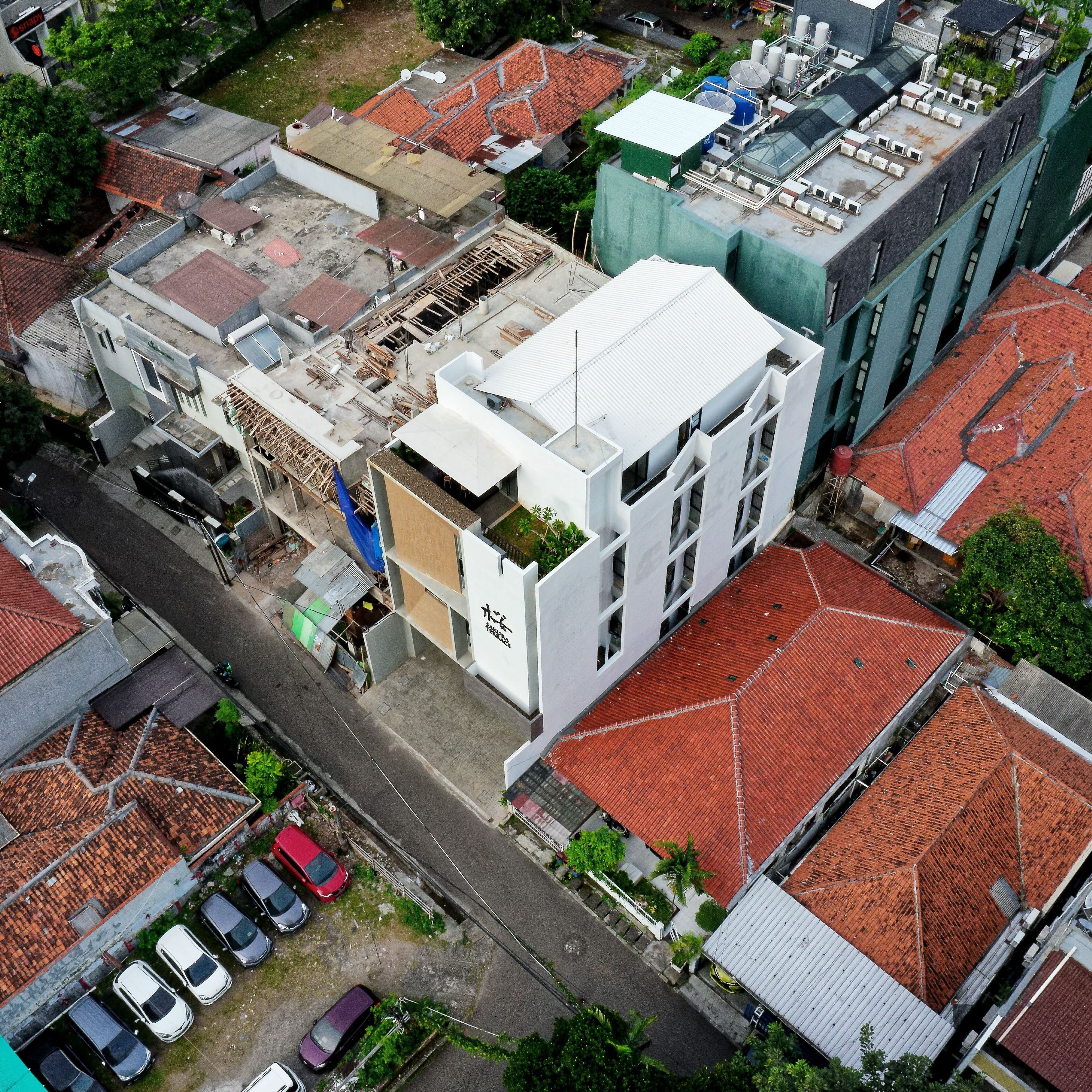 An aerial view of a cityscape with various buildings, including a prominent white building with a flat roof and a green building with a sloped roof.