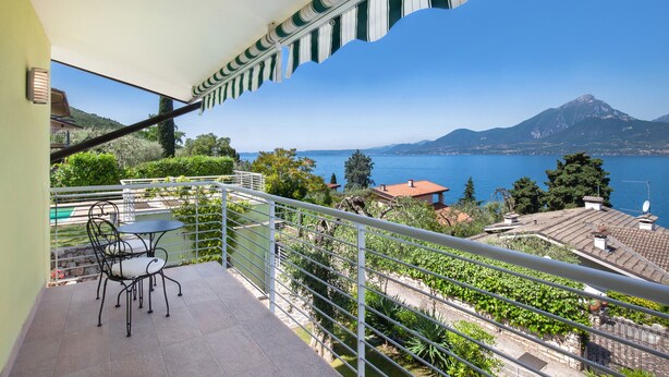 Ein Balkon mit Tisch und Stühlen, mit Blick auf eine Berglandschaft und ein Gewässer.