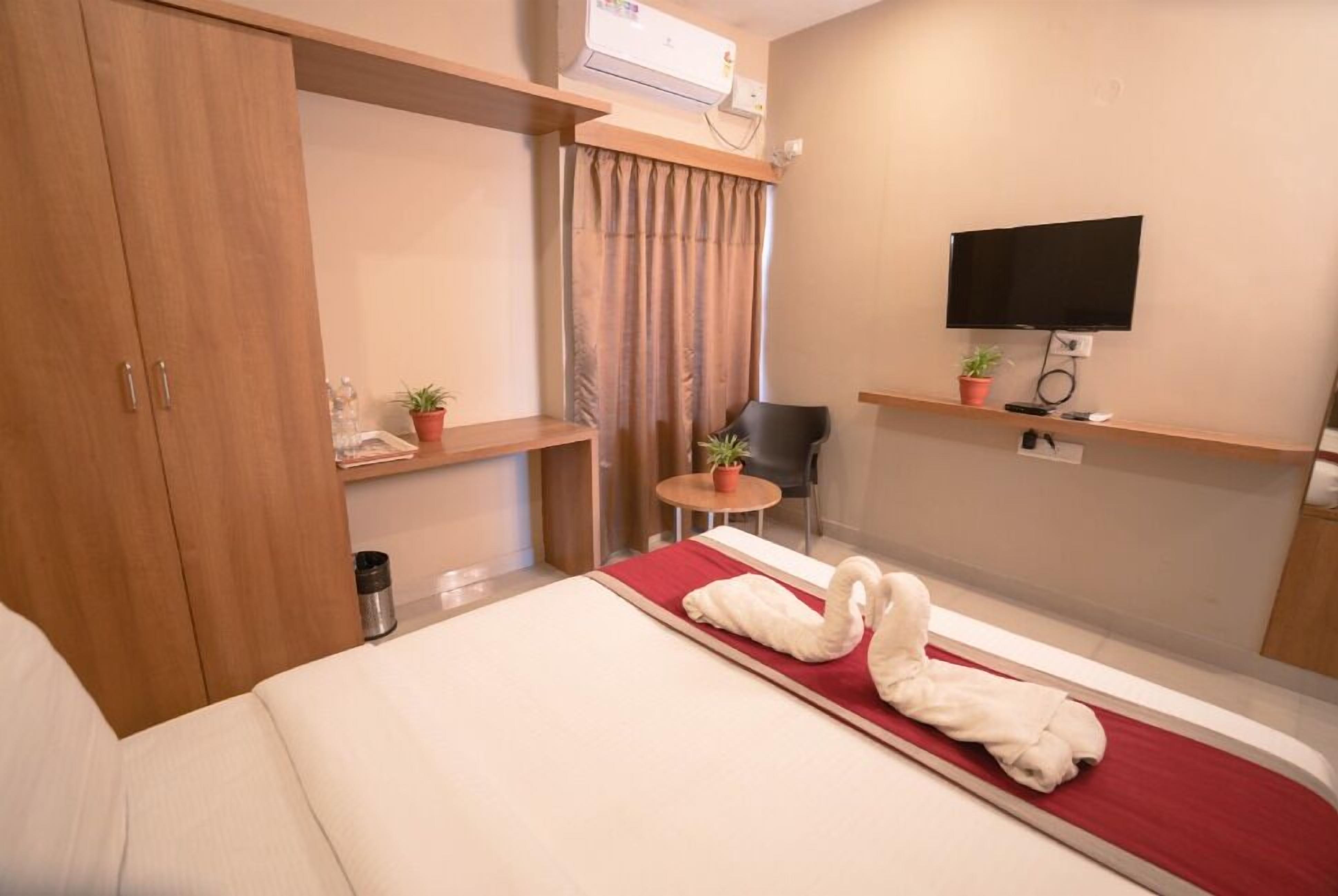 A hotel room with a bed, a TV, a small table with a chair, and a wardrobe.