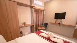 A hotel room with a bed, a TV, a small table with a chair, and a wardrobe. - Samasth Rooms and Suites by YGH (Mysore)