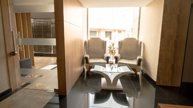 A modern room with a glass coffee table, two armchairs, and a view of the outside. - Samasth Rooms and Suites by YGH (Mysore)