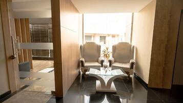 A modern room with a glass coffee table, two armchairs, and a view of the outside.