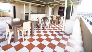 A covered outdoor seating area with a checkered floor, tables, and chairs. - Samasth Rooms and Suites by YGH (Mysore)