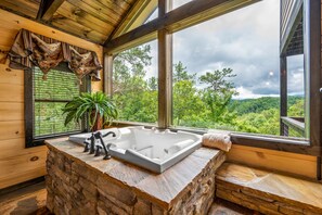 A bathroom with a stone sink, a bathtub, and a view of a forest through large windows. - Now Open The Most  Luxurious Cabin in The Smokies. . Above & Beyond (Sevierville)