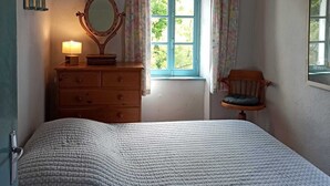 Una camera da letto con un letto, una cassettiera, uno specchio, una finestra con tende e una sedia.