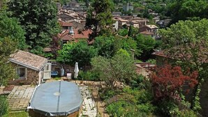 Un cortile con un giardino circolare, mura in pietra e vista su un borgo collinare.