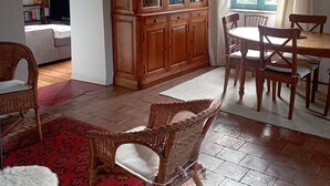 Un accogliente soggiorno con un mobiletto in legno, poltrone in vimini, un tappeto rosso decorato e un tavolo da pranzo con sedie.