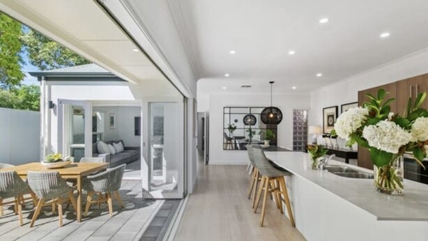 A modern kitchen with a central island, a dining area with a wooden table and chairs, and a view of a garden through large windows. - Sandstone Villa In City Fringe Location (Fullarton)