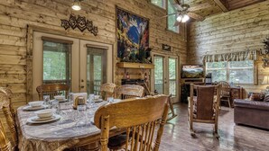 A wooden interior with a dining table set for four, a sofa, and a television.