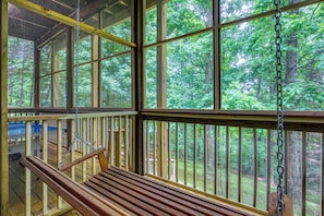 Eine Holzterrasse mit Schaukel, großen Fenstern und Blick auf einen Wald.