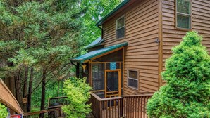 A wooden cabin with a deck, surrounded by dense forest.