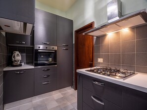 Een moderne keuken met donkere kastjes, een inbouwoven, een koffieapparaat en een gasfornuis.
