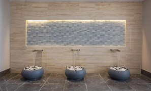 A modern bathroom with a tiled wall, three water features, and marble flooring.