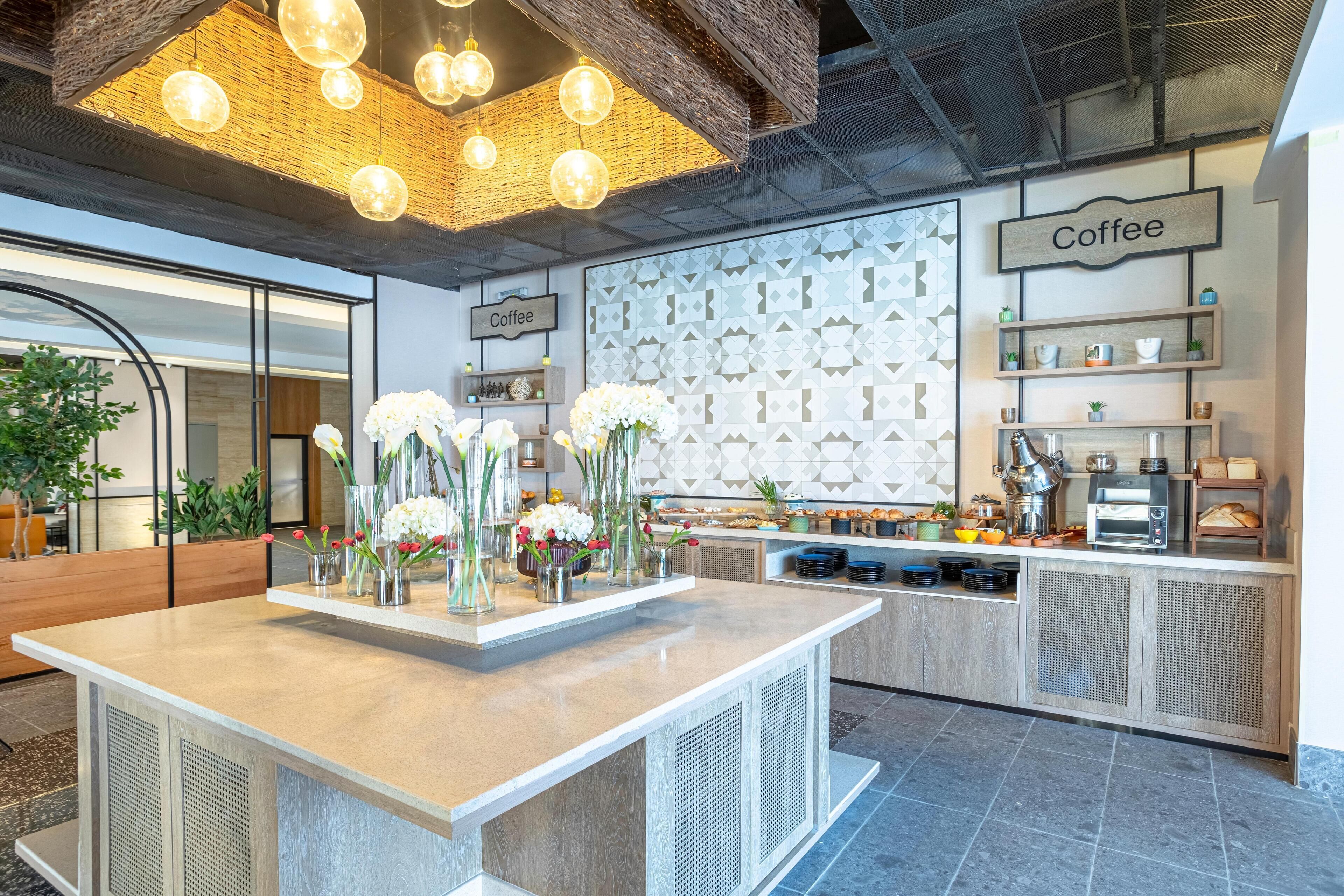 Ein modernes Café-Interieur mit einer zentralen Theke, hängenden, kugelförmigen Leuchten und einer Wand mit geometrischem Muster.