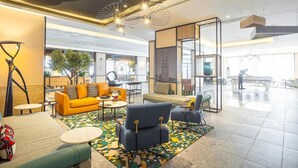 Eine großzügige Lobby mit modernem Design, inklusive eines gelben Sofas, blauer Sessel und einem gemusterten Teppich.