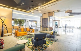A spacious lobby with a modern design, featuring a yellow sofa, blue armchairs, and a patterned rug.