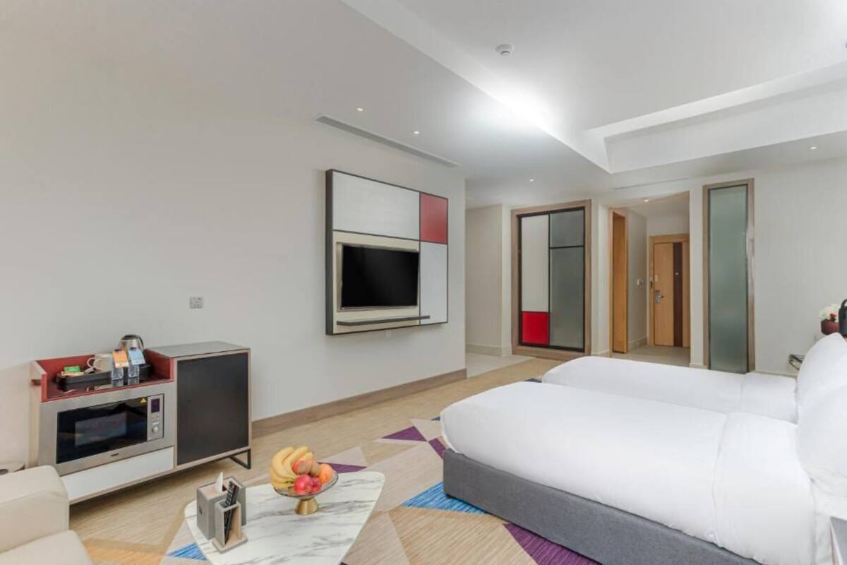A modern hotel room with a large bed, a flat-screen TV, a microwave, and a small kitchenette.