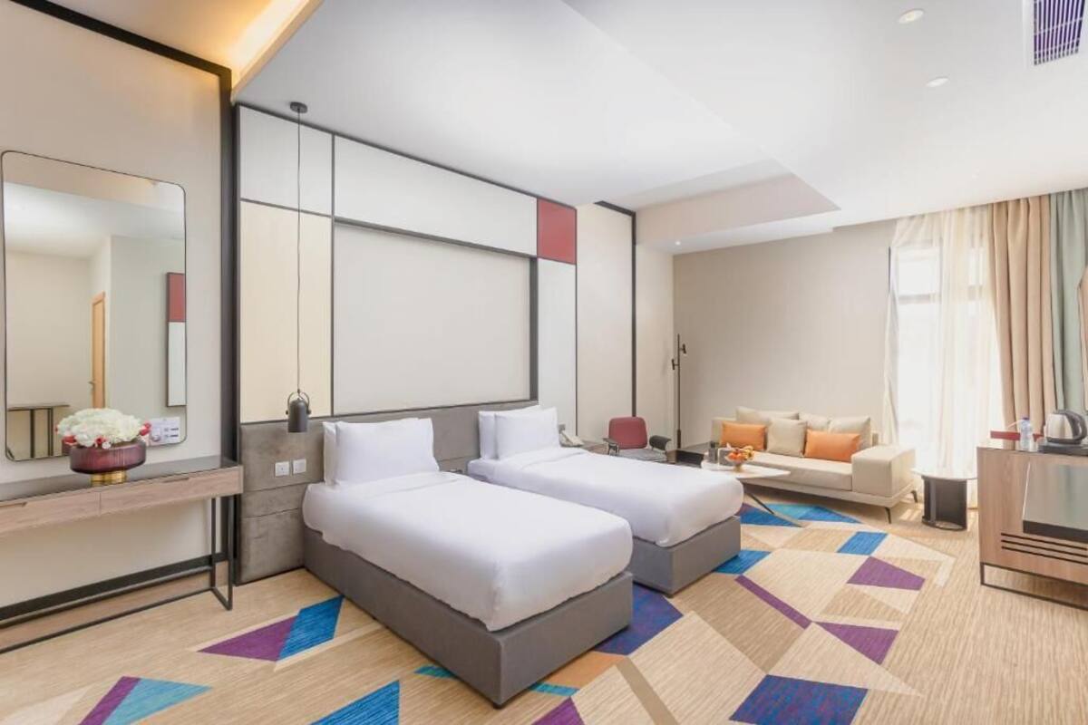 A hotel room with two beds, a sofa, a desk, and a TV.