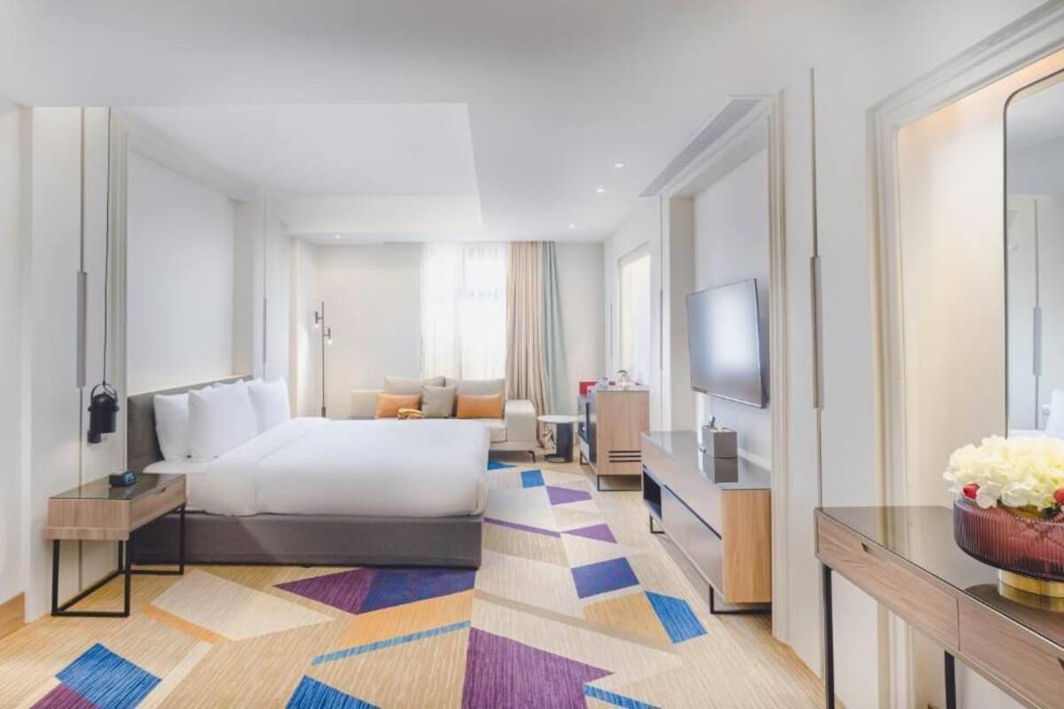 A modern hotel room with a large bed, a desk, a television, and a mirror.