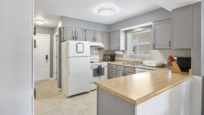 A modern kitchen with white appliances, grey cabinets, and a wooden countertop.