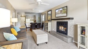 A living room with a fireplace, a dining area, and a kitchen in the background.