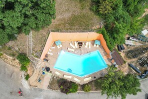 An aerial view of a swimming pool area with a fenced deck, lounge chairs, and a small building.