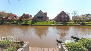 Een gracht met huizen aan één kant en een houten steiger met een bankje.