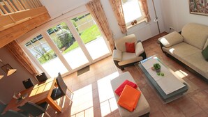 Een woonkamer met een bank, fauteuils, een salontafel en een eethoek met stoelen en een tafel.