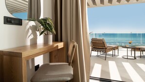 Habitació moderna amb escriptori de fusta, una cadira, una planta en test i vista a l'oceà a través de grans finestres.