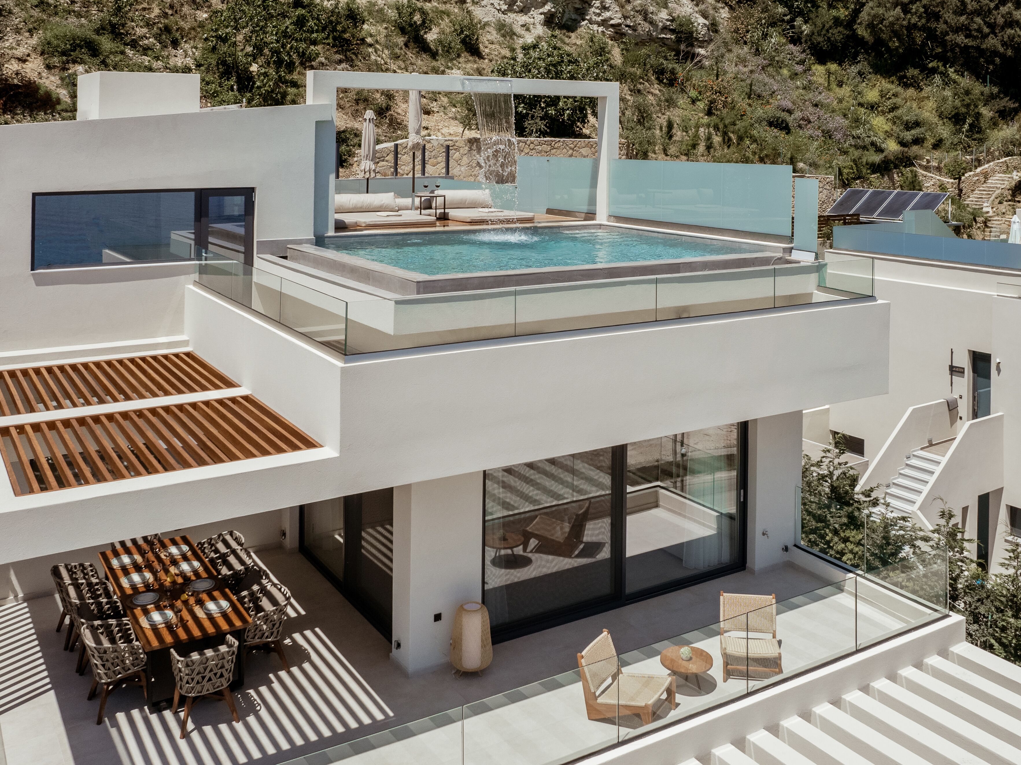 Ein modernes, zweistöckiges Gebäude mit Pool auf dem Dach, Sitzgelegenheiten im Freien und einer Treppe, die zur oberen Ebene führt.