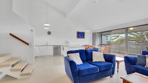 Relax in the living area with a sofa and armchair, overlooking a balcony with a view of palm trees.