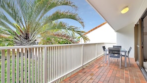 Enjoy the serene garden views from this balcony with a table and chairs under a shaded area.