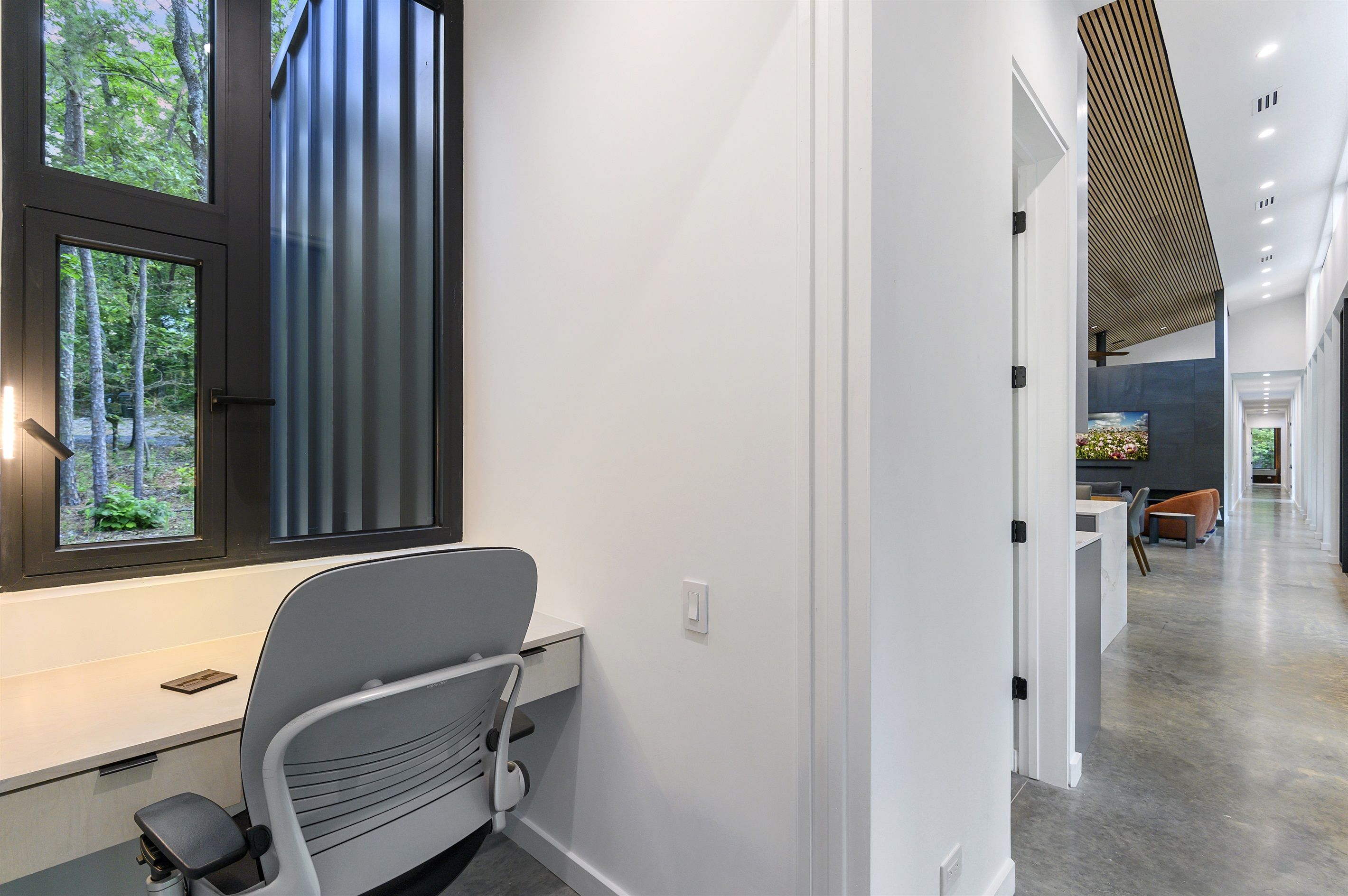A modern interior with a desk, chair, and large window overlooking a forest.