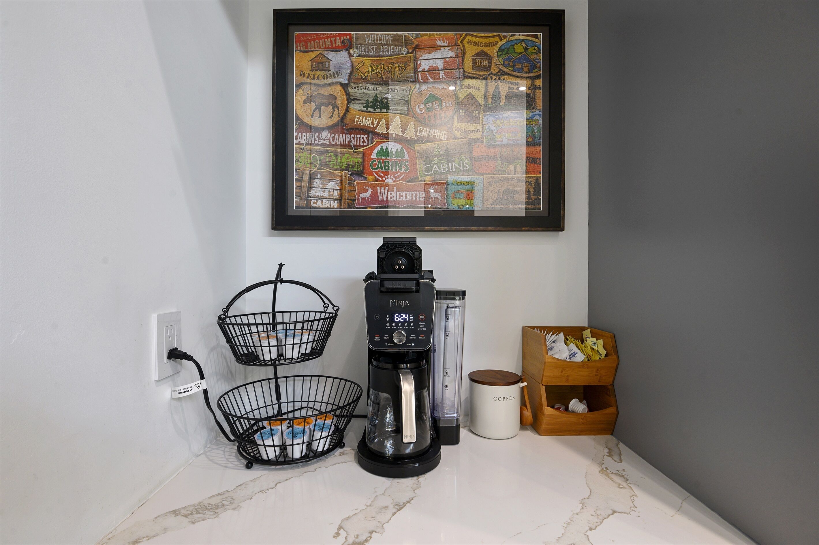 Un coin cuisine équipé d’une machine à café, de deux paniers, d’une tasse et d’un panneau d’accueil encadré.