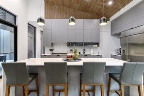 Cozinha moderna com ilha central, cadeiras cinzas e eletrodomésticos de aço inoxidável.