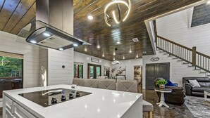 A modern kitchen with a central island, a dining area with a sofa, and a staircase leading to a loft bedroom. - Family Retreat with Game Room and Playset (Broken Bow)