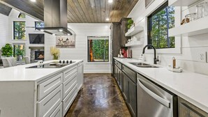 A modern kitchen with white cabinetry, a central island, a built-in stove, and a large window offering a view of the outdoors. - Family Retreat with Game Room and Playset (Broken Bow)