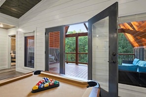 Een kamer met een pooltafel, uitzicht op een terras met tuinmeubilair en een groot raam.