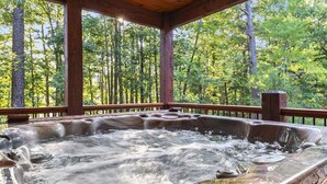 A hot tub surrounded by a wooden deck with a forest view. - Family Retreat with Game Room and Playset (Broken Bow)