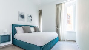 A modern bedroom with a teal bed, white bedding, and two wall art pieces.