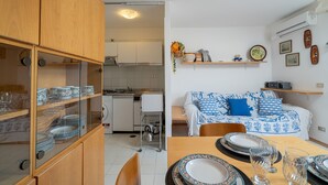A compact kitchen with a dining area, a sofa with patterned cushions, and a small shelf with decorative items. - Rena Bianca House by Wonderful Italy (Olbia)
