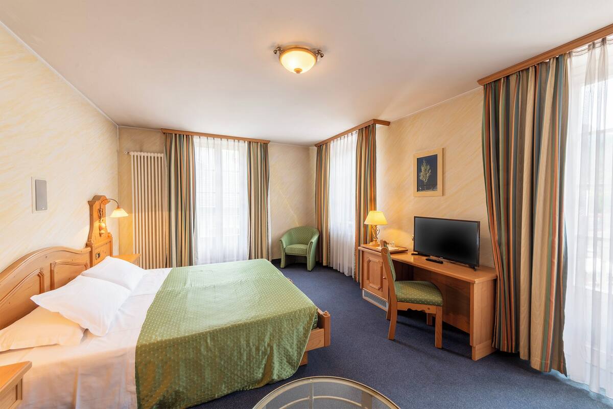 Ein Hotelzimmer mit Bett, Schreibtisch, Stuhl, Fernseher und Vorhängen.