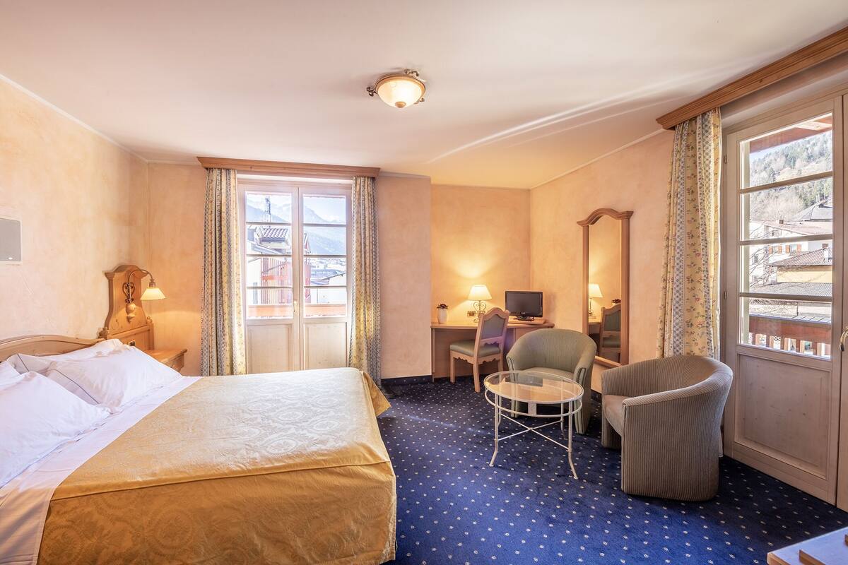 Ein Hotelzimmer mit einem Bett, einem Schreibtisch mit Computer, einem Stuhl und Blick auf einen Berg.