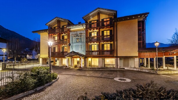 Un hôtel à plusieurs étages, avec une entrée centrale, un bar situé sur le côté droit et une vue sur les montagnes en arrière-plan.