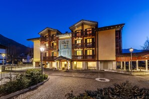 Un hôtel à plusieurs étages, avec une entrée centrale, un bar situé sur le côté droit et une vue sur les montagnes en arrière-plan.