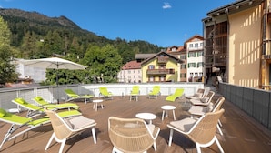 Une terrasse sur le toit, dotée de chaises et de tables en osier, offrant une vue sur un paysage montagneux.