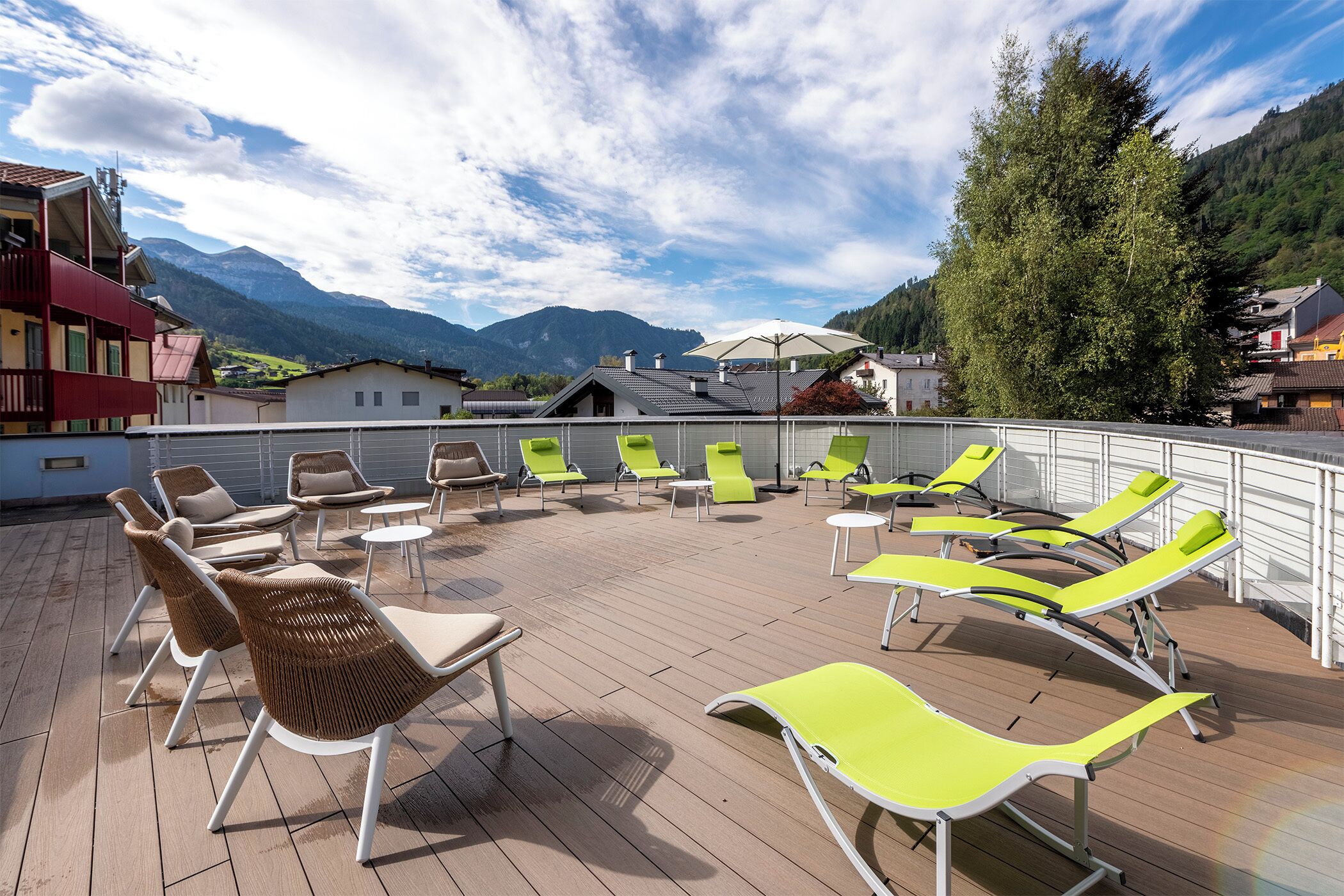 A rooftop terrace with multiple lounge chairs and tables, overlooking a mountainous landscape.