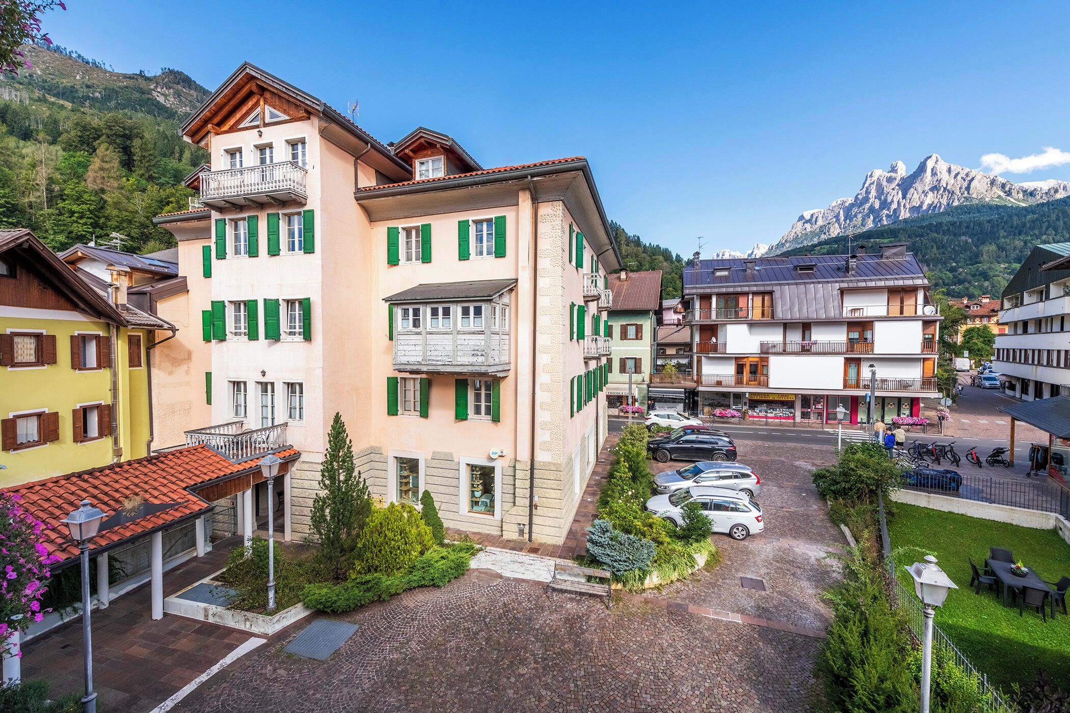 A multi-story building with balconies, a parking area, and a mountain backdrop.