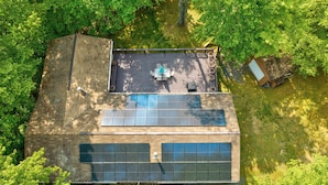 Uma casa moderna com terraço no telhado, painéis solares e um pequeno galinheiro.